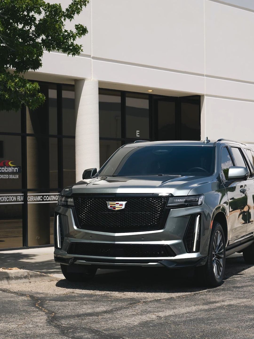 A silver cadillac escalade is parked in front of a building.
