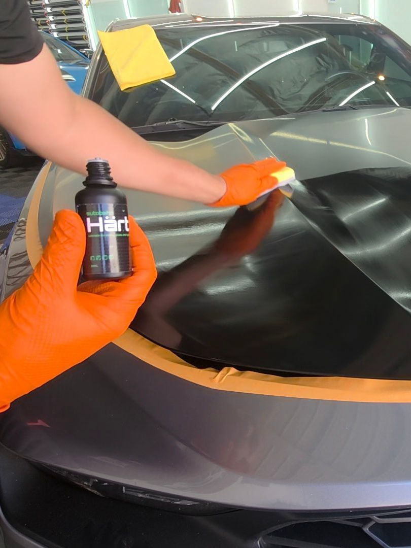 A person wearing orange gloves is wrapping a car