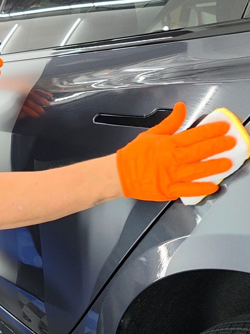 A person wearing orange gloves is cleaning a car with a sponge.