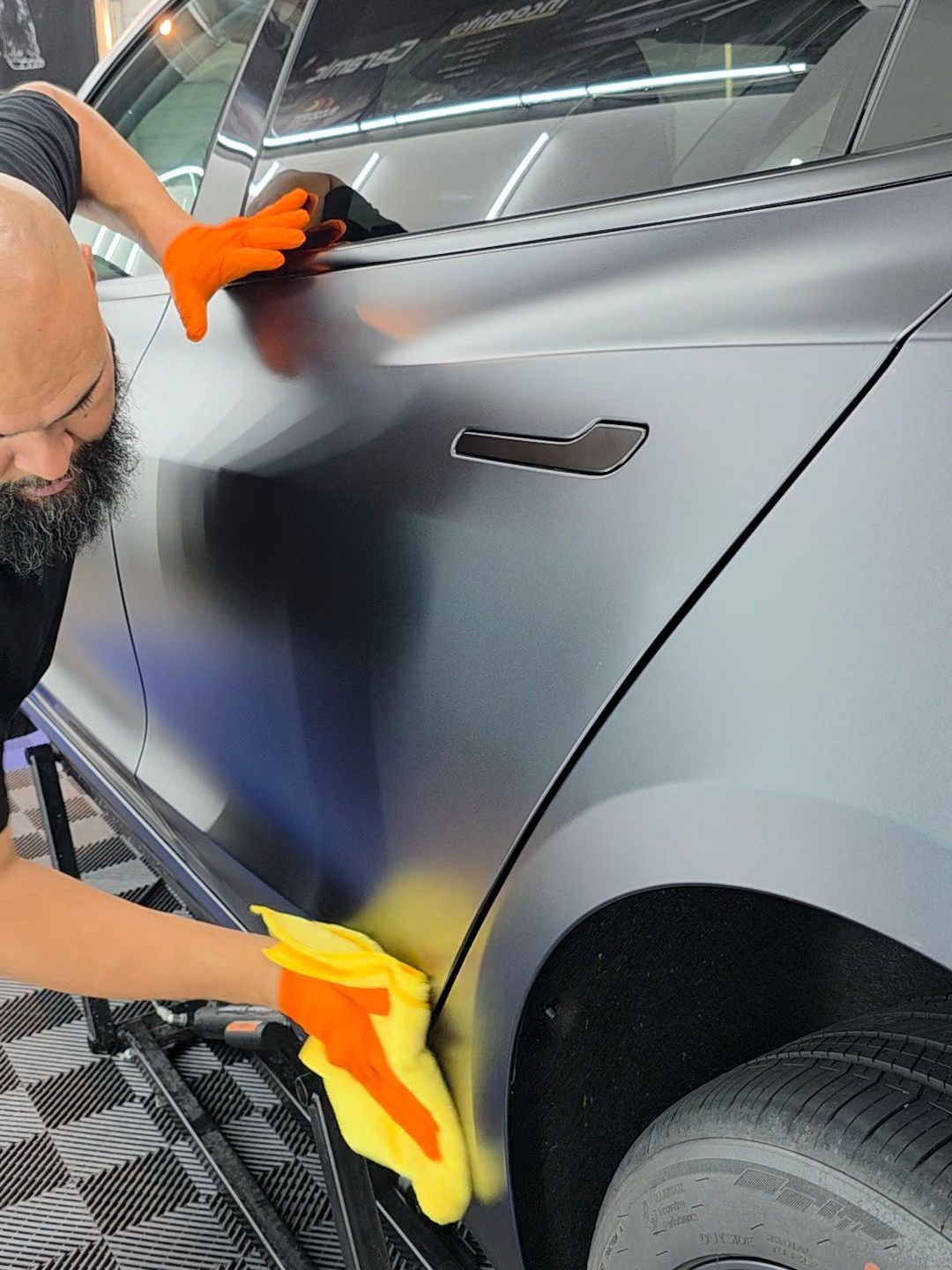 A man is cleaning the side of a car with a yellow cloth.