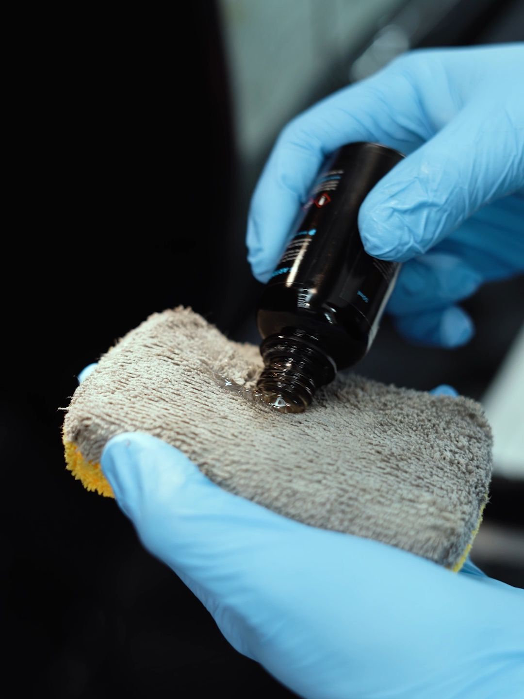 A person wearing blue gloves is cleaning a sponge with a bottle of liquid.