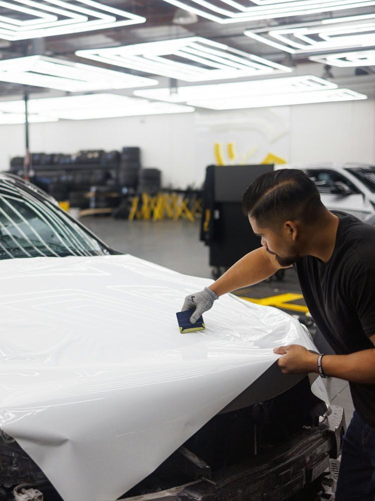 A man is wrapping the hood of a white car in a garage.