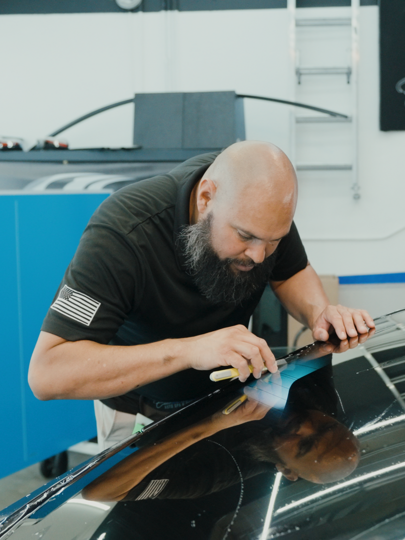 A man with a beard is cleaning the windshield of a car.