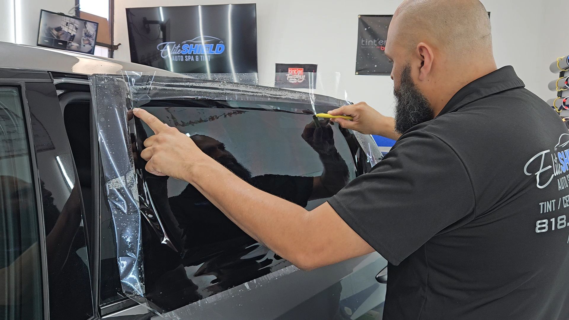A man is wrapping a car window with plastic wrap.