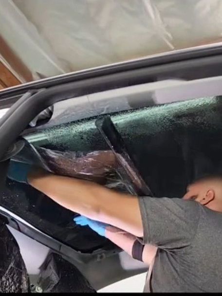 A man is applying window tinting to a car window.