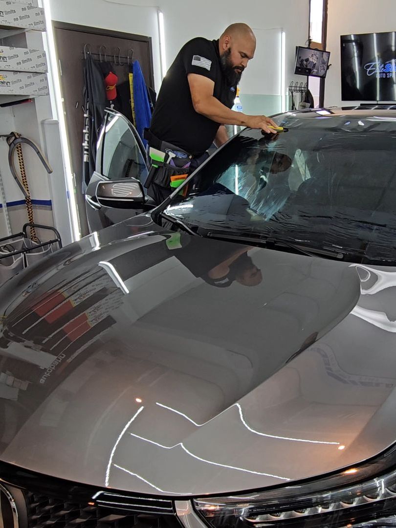 A man is cleaning the windshield of a car in a garage.
