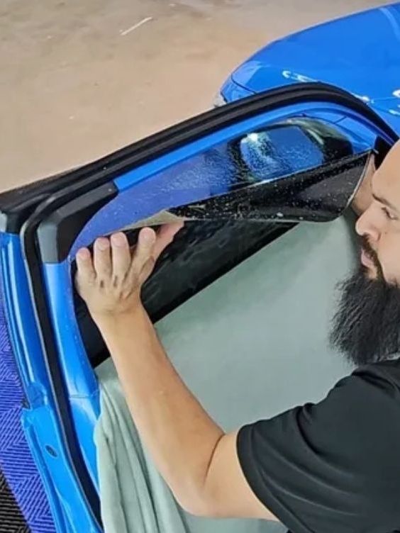 A man with a beard is working on a blue car
