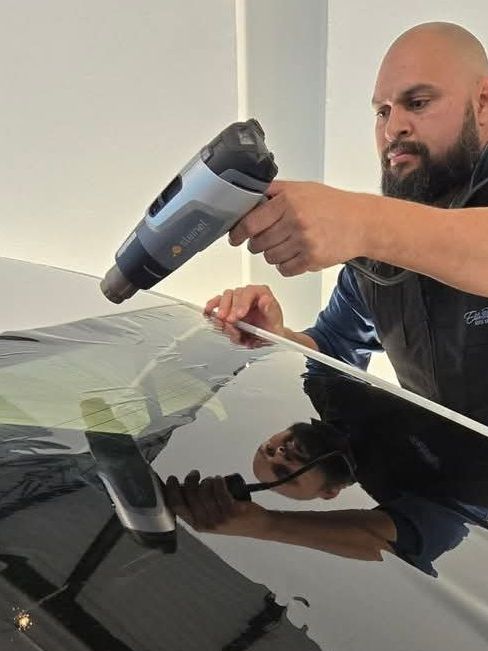 A person wearing black gloves is polishing the hood of a red car.