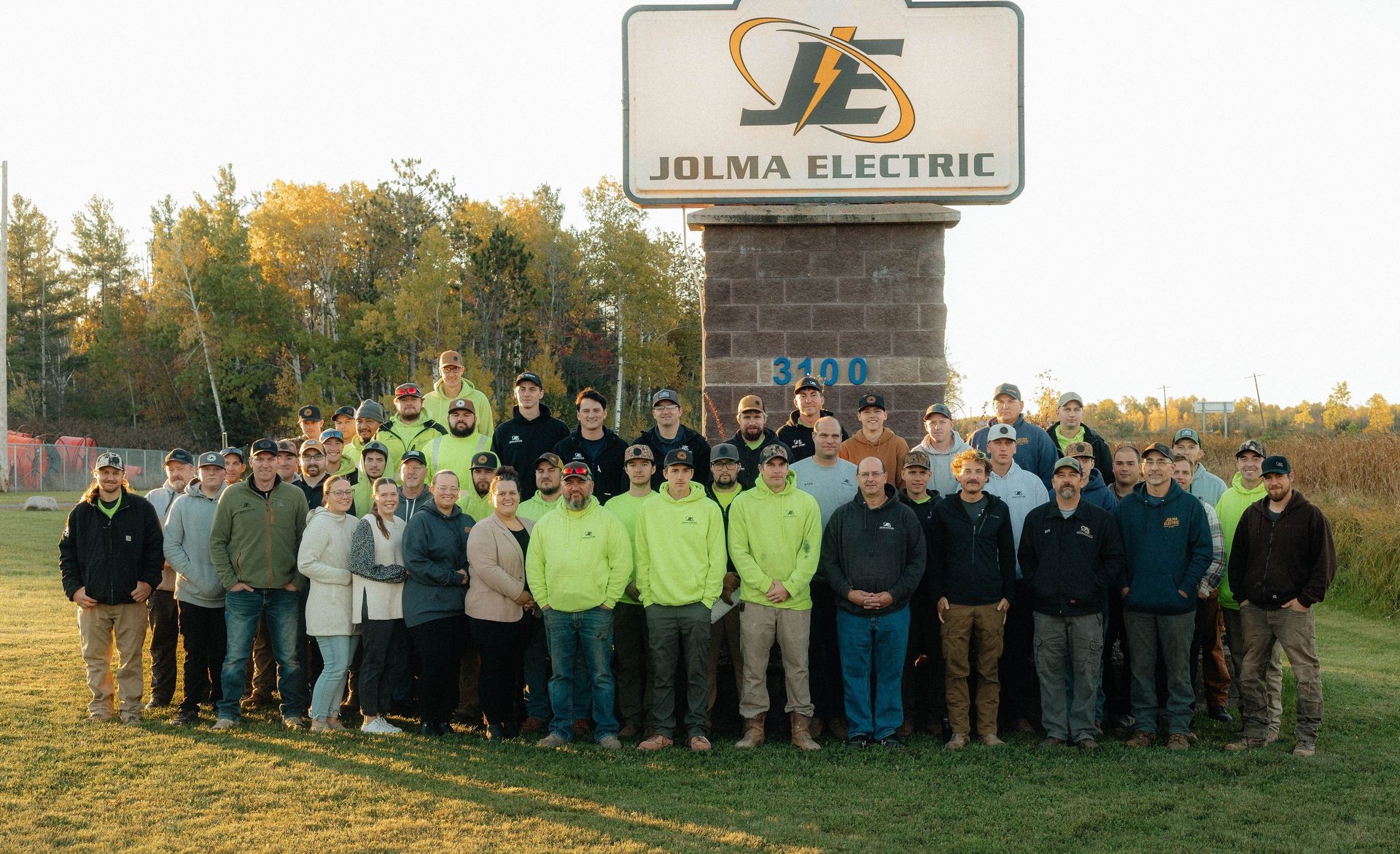 A worker in a high-visibility long-sleeve shirt and hard hat installs wiring in an electrical control panel.
