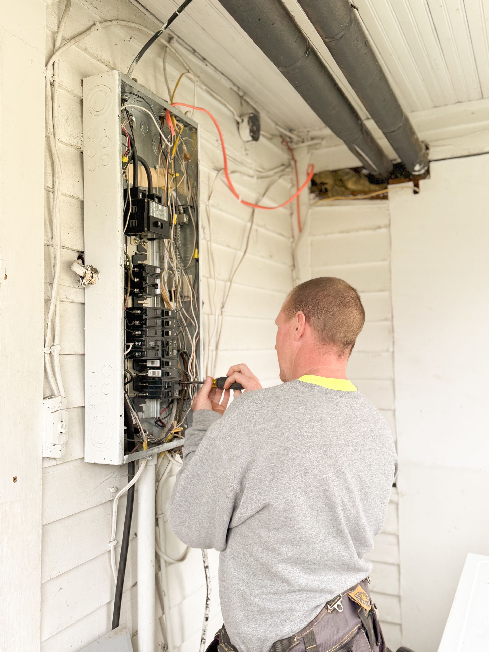 A technician in gloves uses a multimeter probe to test electrical components inside a control panel cabinet.