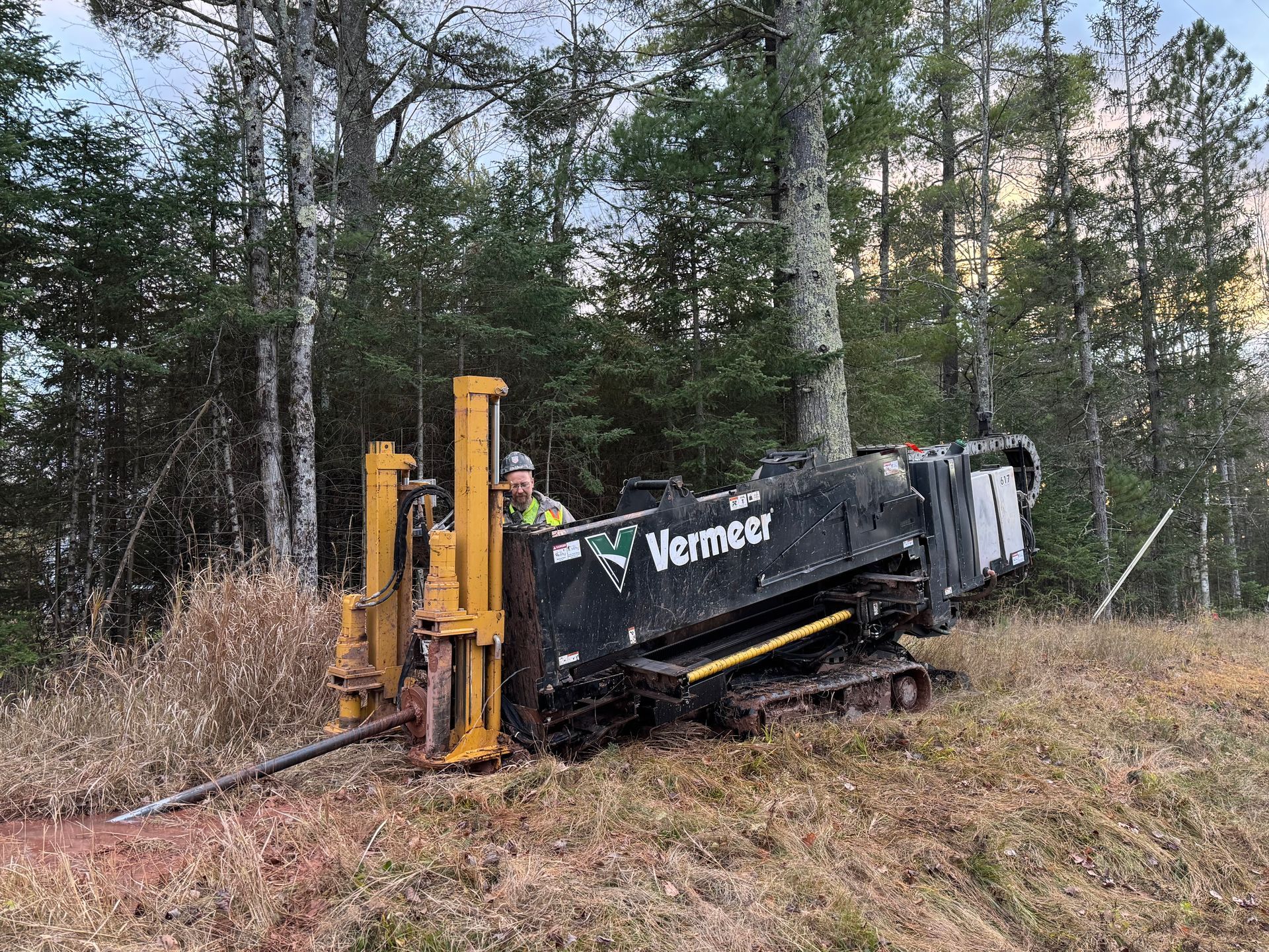 A yellow and black Vermeer horizontal directional drill operates on a hillside in a forest. A yellow and black Vermeer horizontal directional drill operates on a hillside in a forest.