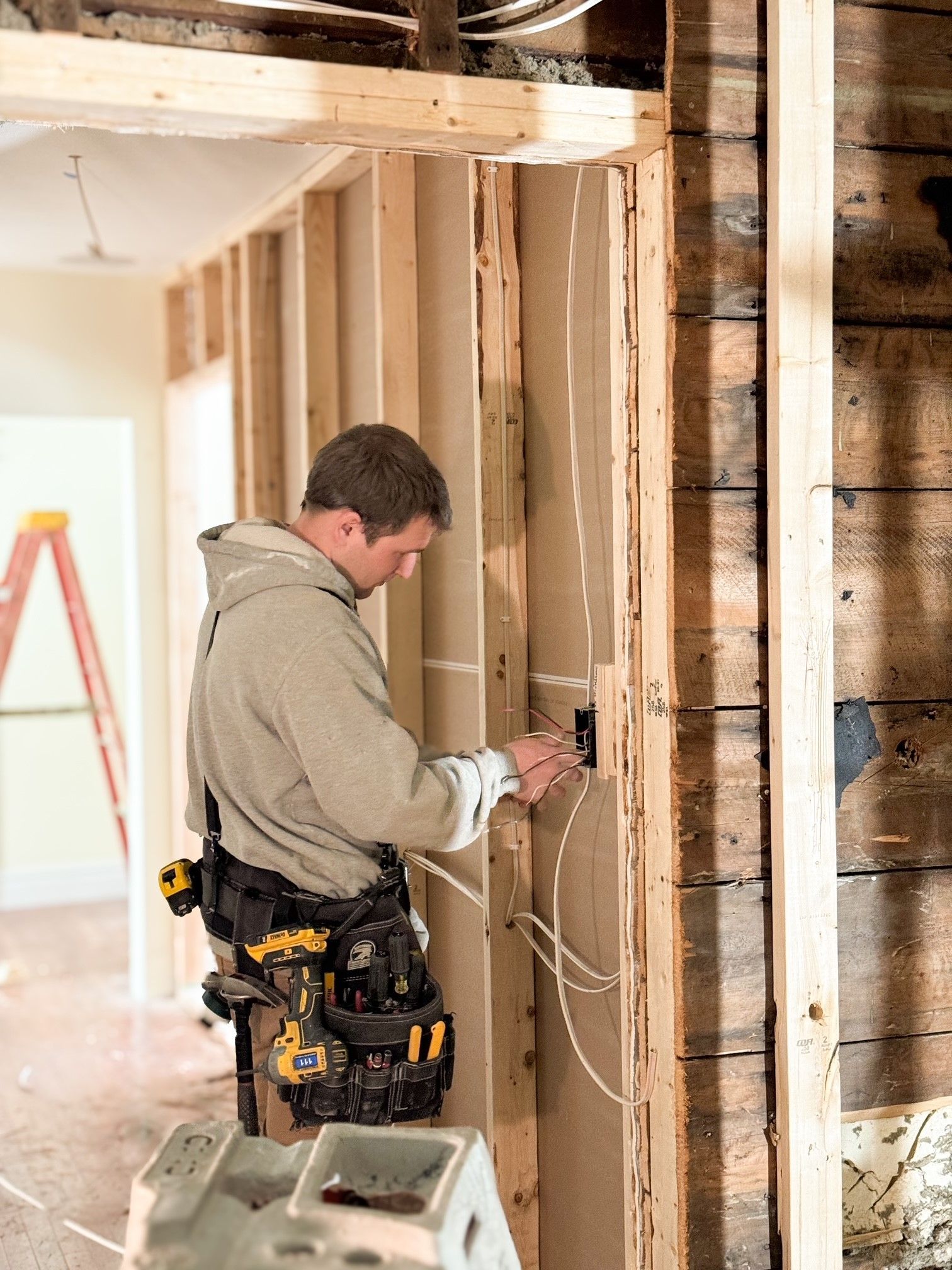 A person wearing a tool belt installs electrical wiring into a stud wall in a room under construction.