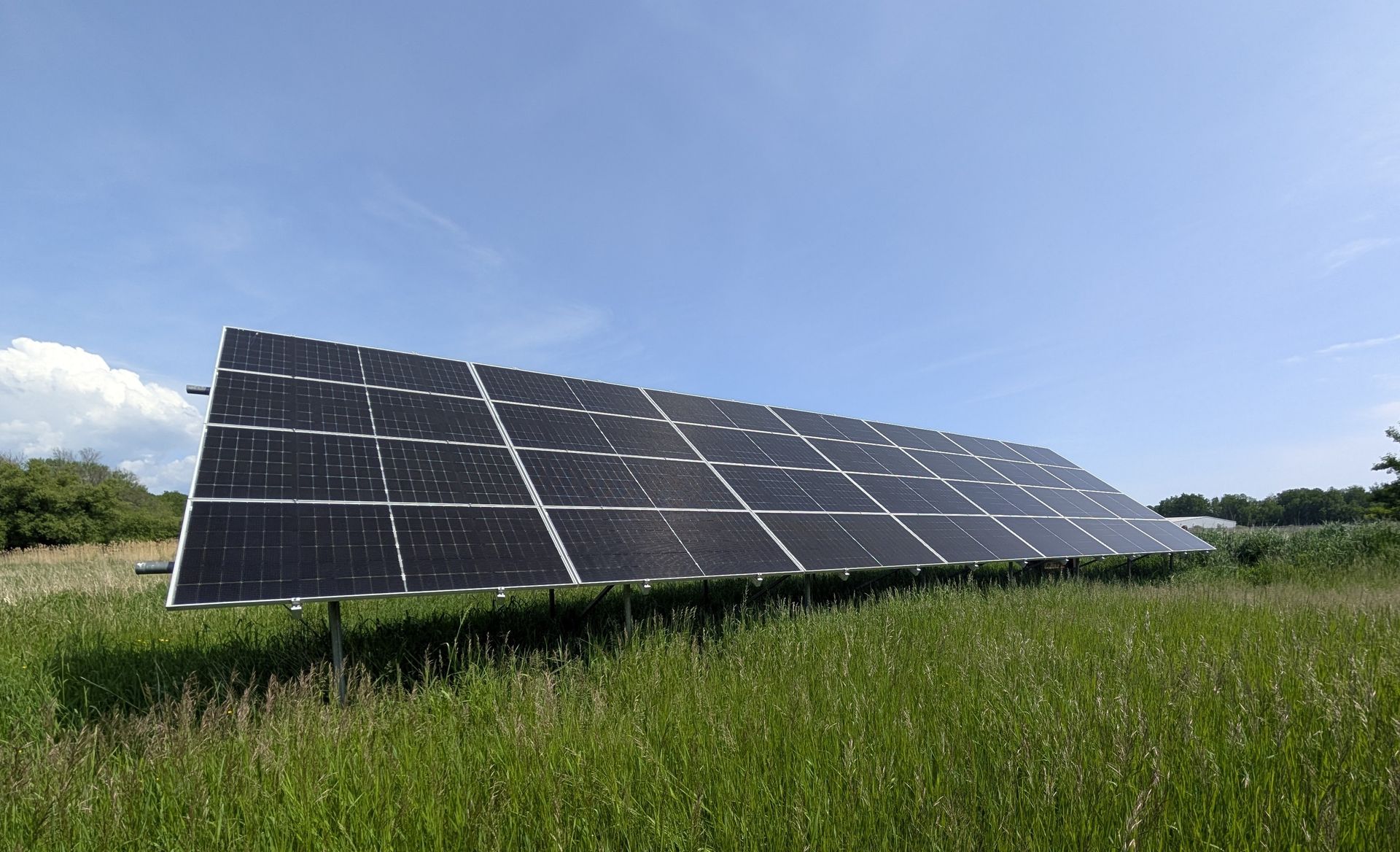 A person in a beanie and work harness installs a solar panel onto a bright red metal roof against a cloudy sky.