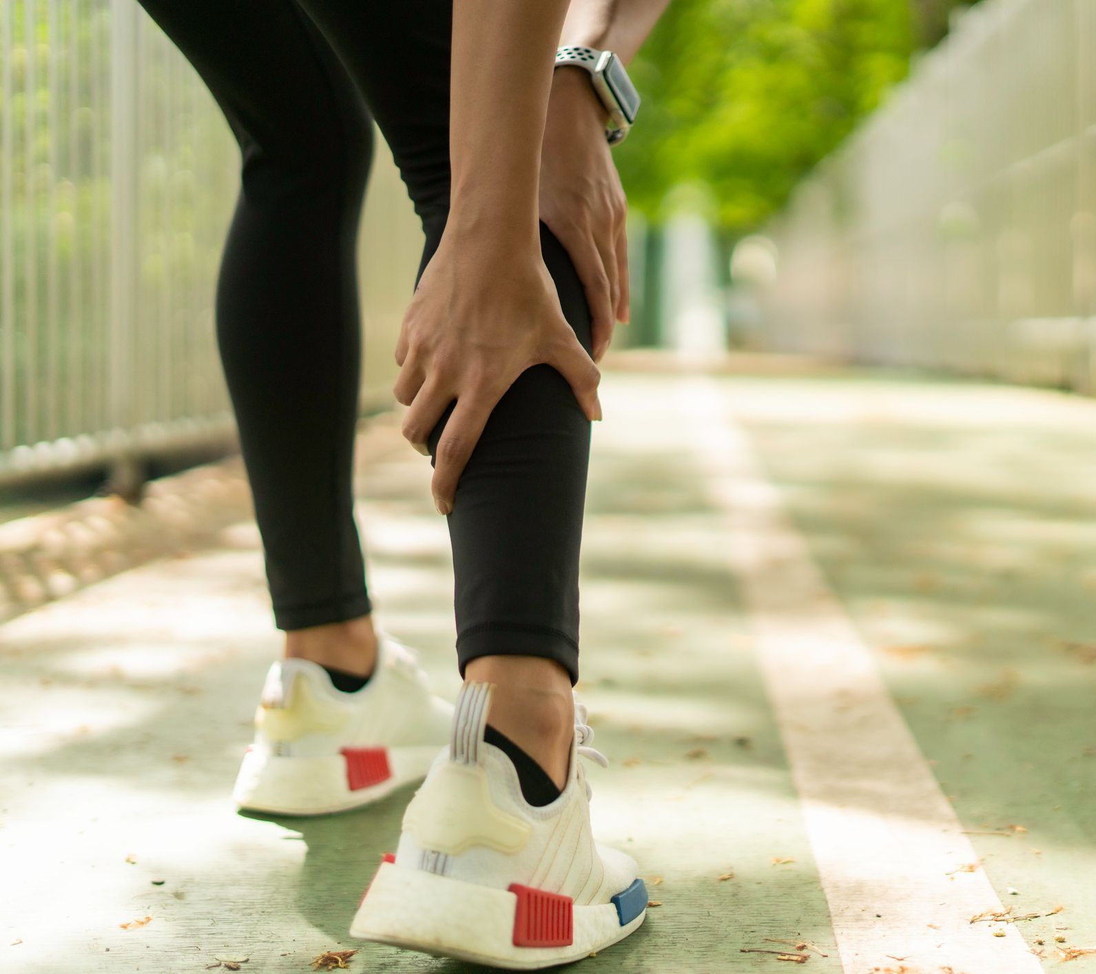 Person holding their leg, likely due to pain, on an outdoor running track.