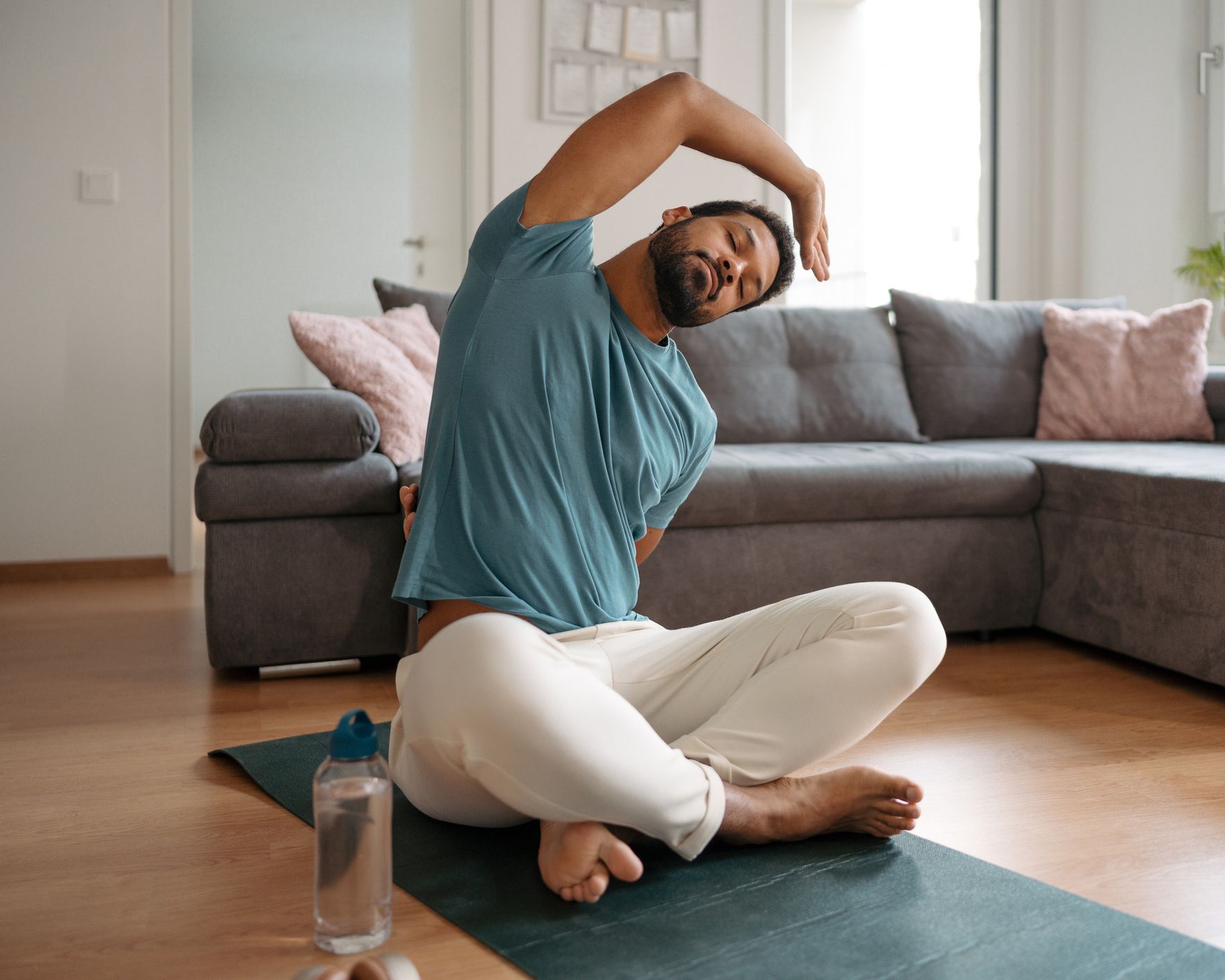 Man in casual clothes stretching on a yoga mat in a living room.