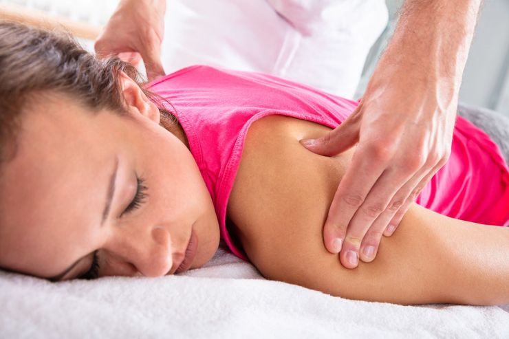 Woman receiving shoulder massage, lying face down on a white towel, pink shirt.