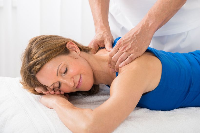 Woman receiving a shoulder massage; hands of masseuse on her neck. She is lying down, eyes closed.