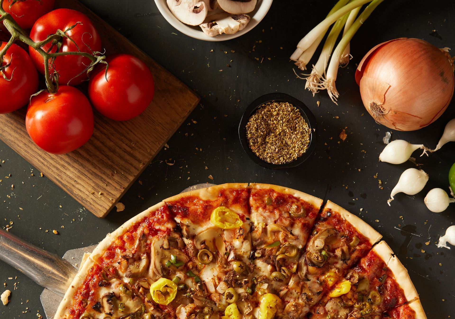 A pizza is surrounded by vegetables and tomatoes on a table.