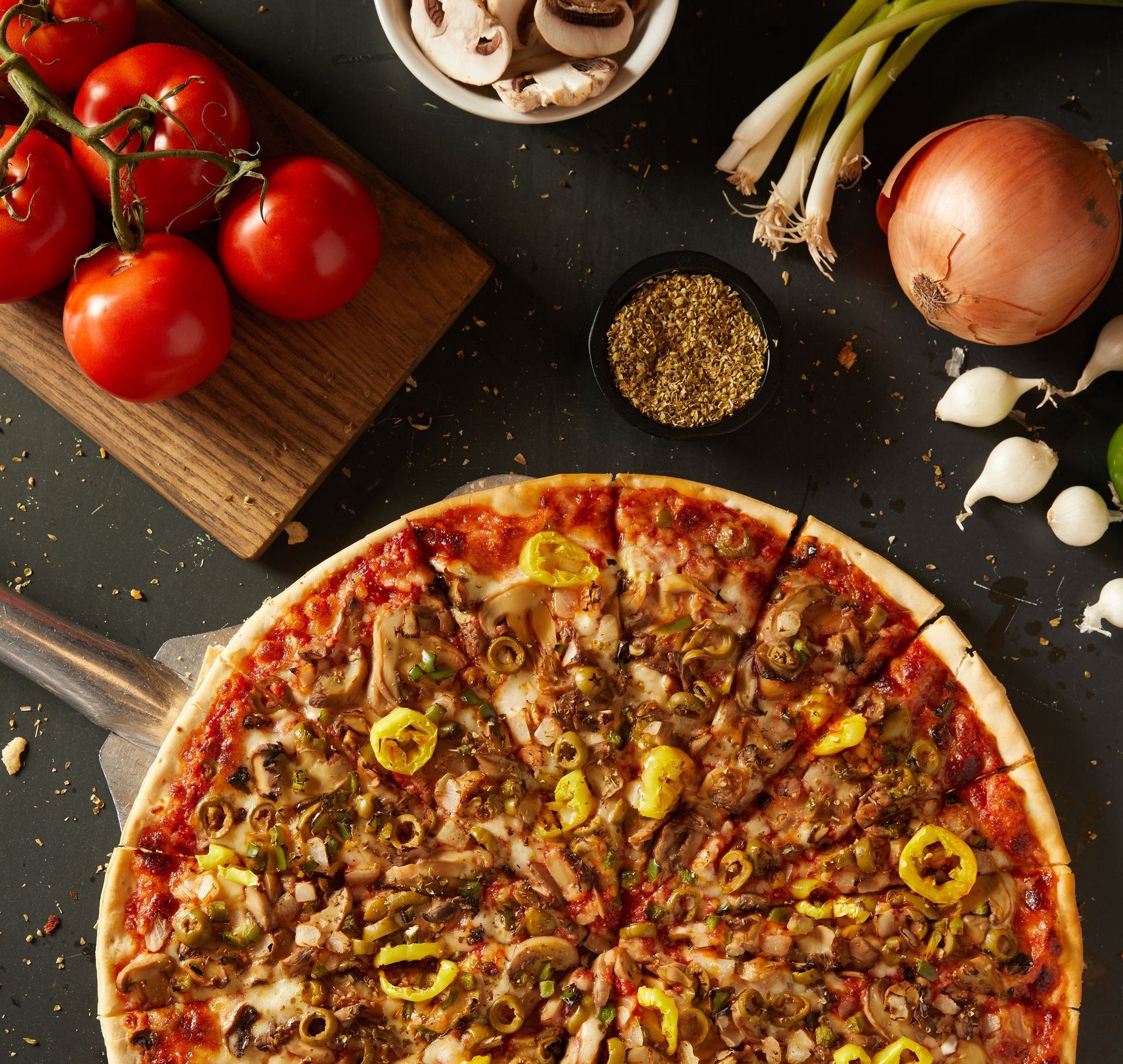 A pizza surrounded by vegetables and tomatoes on a table