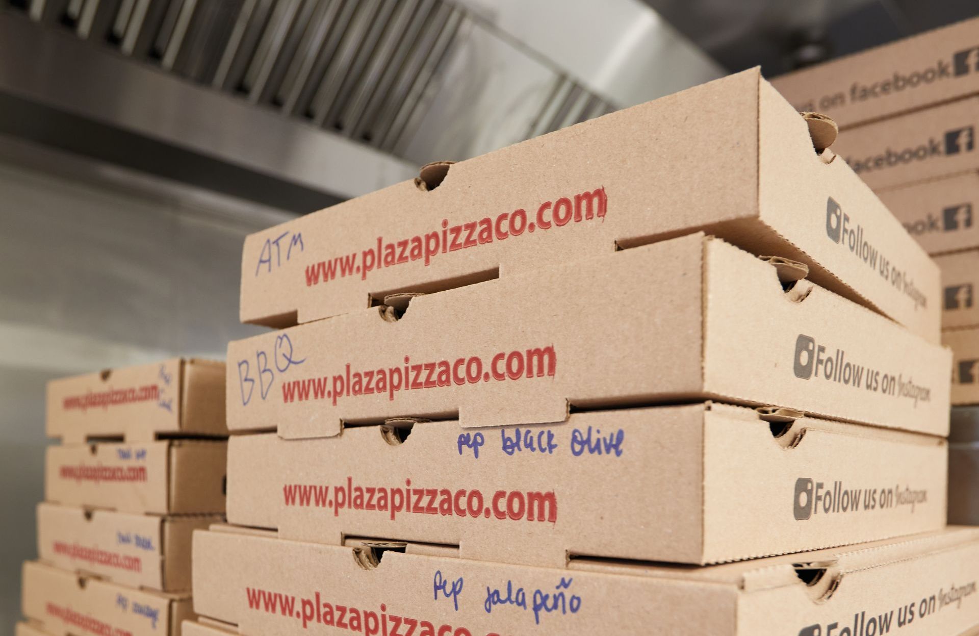 A stack of pizza boxes that say www.plazapizzaco.com