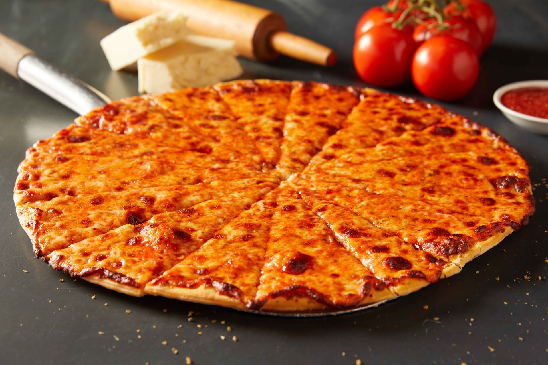 A pizza is sitting on a pan on a table next to tomatoes and cheese.