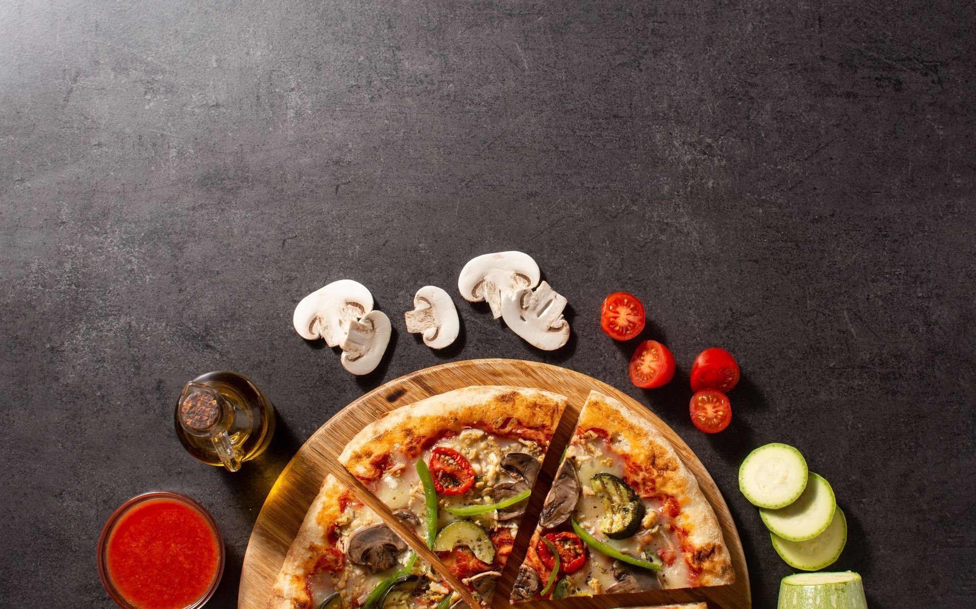 A pizza is sitting on a wooden cutting board on a table surrounded by vegetables.