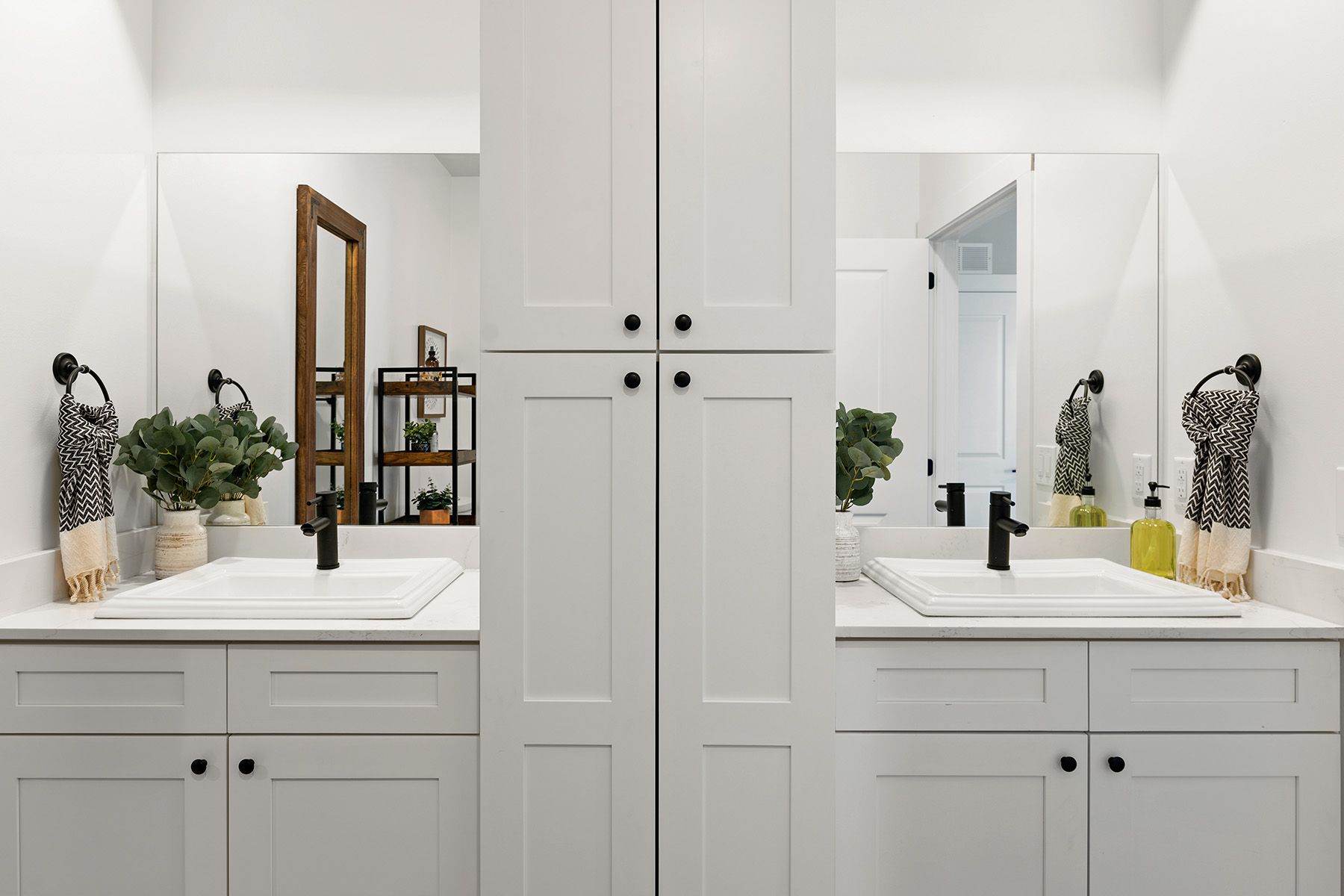 An image of Pointe Grand Columbia Apartment Homes' bathroom with a double vanity sink, white cabinets, oversized mirrors, a dress mirror, and towel hangers.
