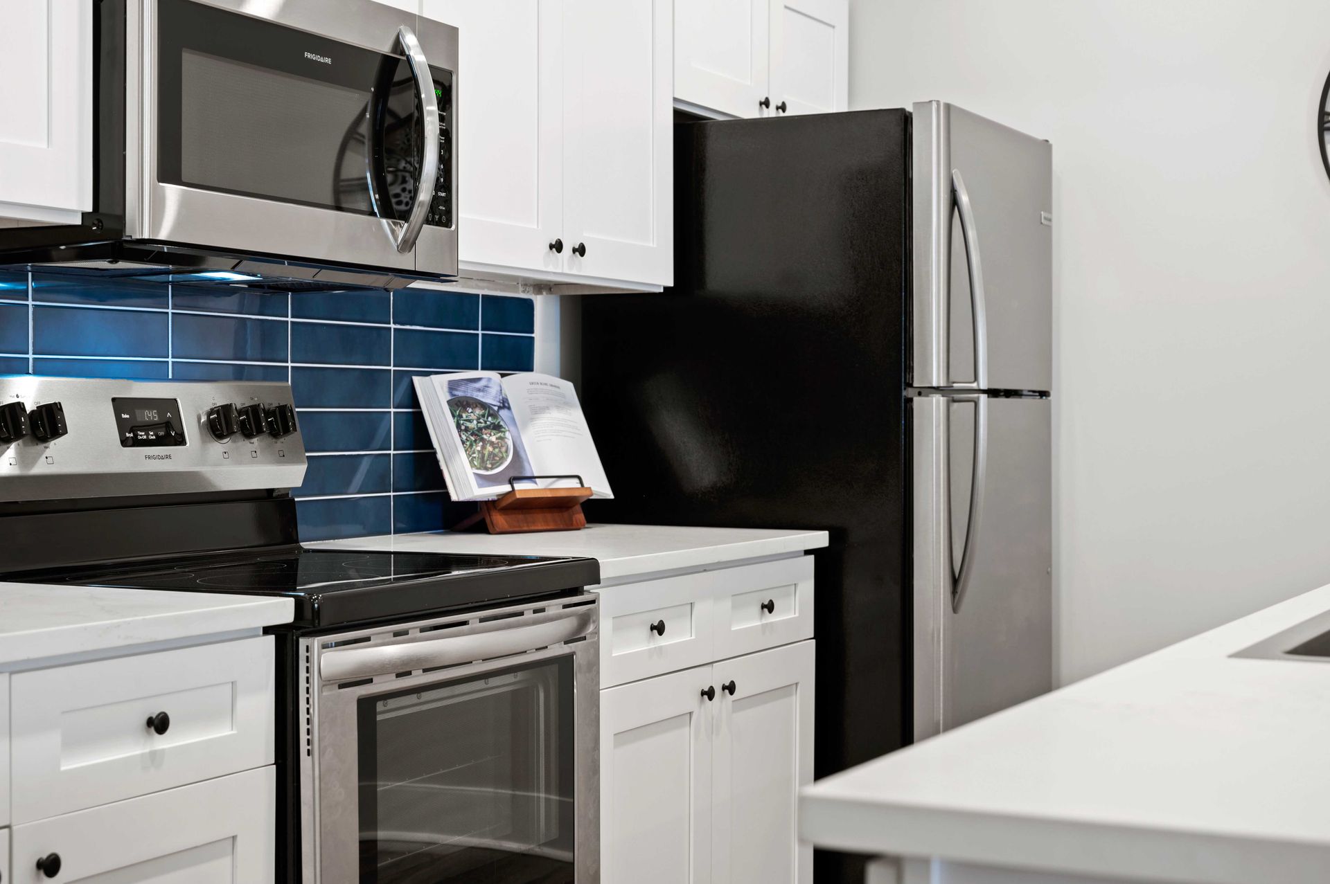 A close shot of Pointe Grand Columbia Apartment Homes' kitchen with an island, bar chairs, white cabinets, stainless steel appliances, and a blue tile backsplash.
