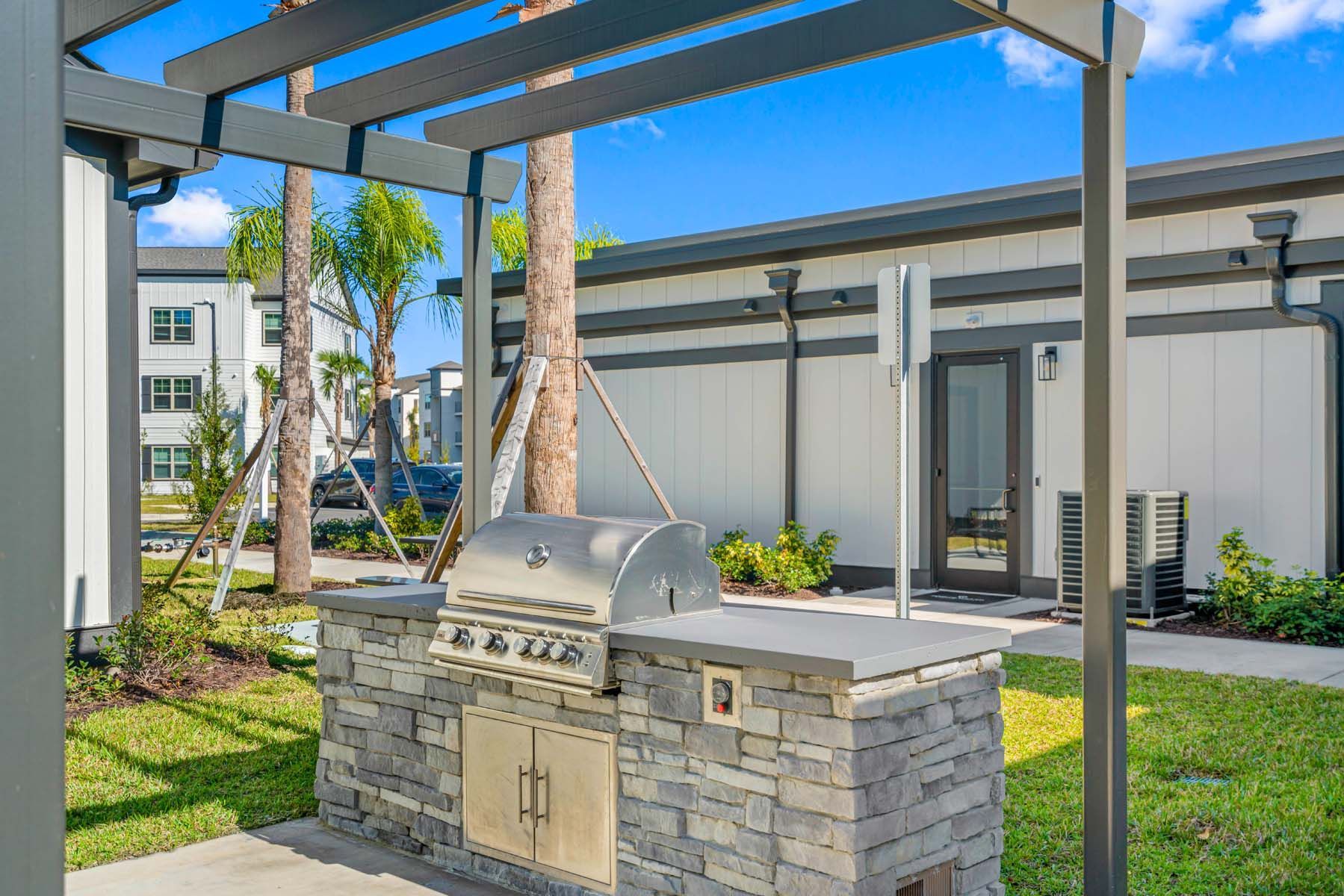 A grill is sitting under a pergola in front of a building at Pointe Grand Columbia apartments in Columbia, SC.