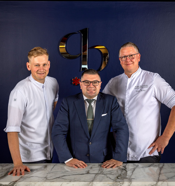 Three men are standing next to each other in a kitchen.