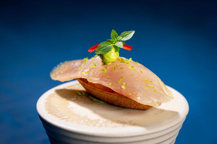 Small appetizer: raw fish on toasted bread, topped with sauce, lime zest, mint, and chili.