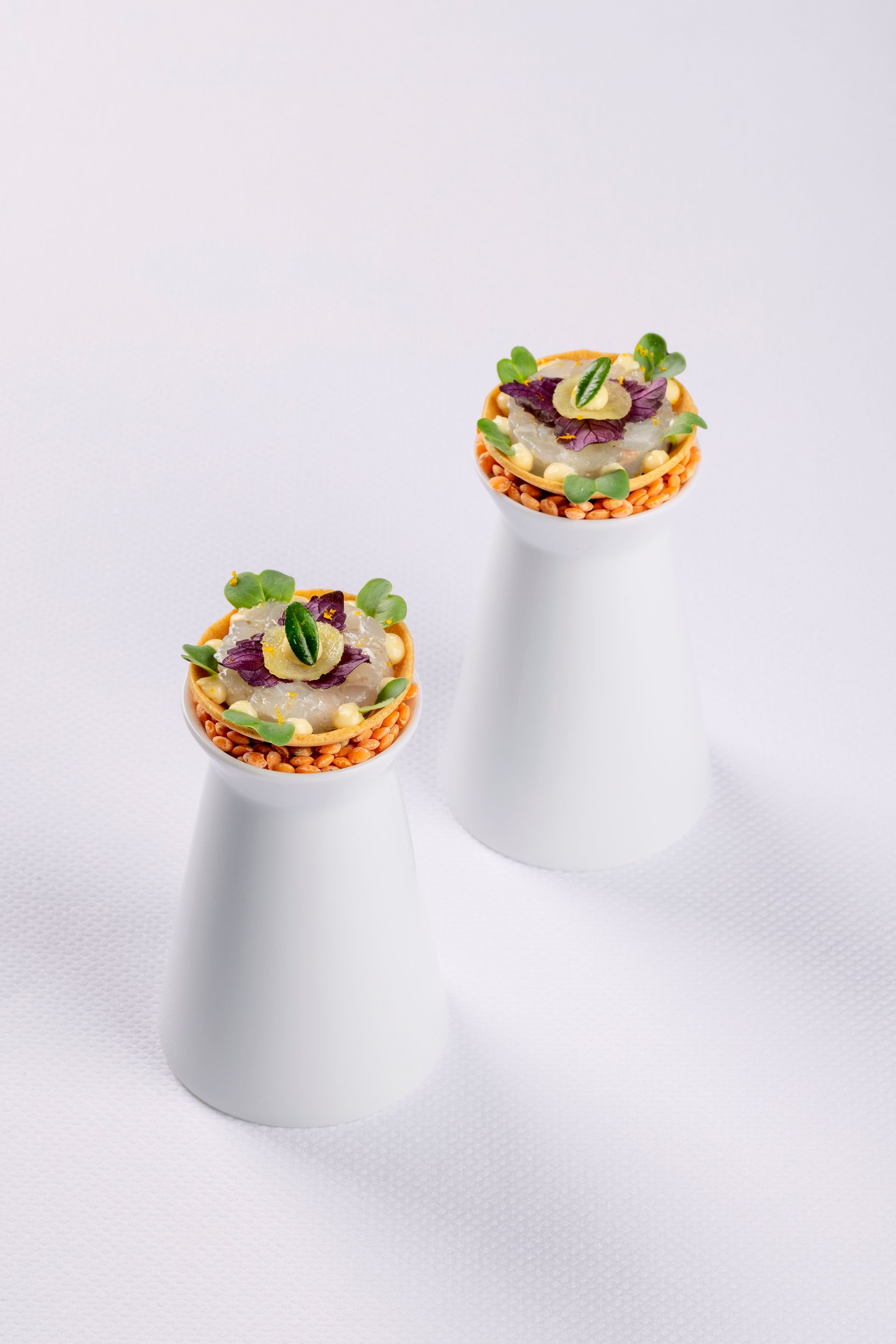 Twee witte zout- en peperstrooiers met eten erop op een wit oppervlak.