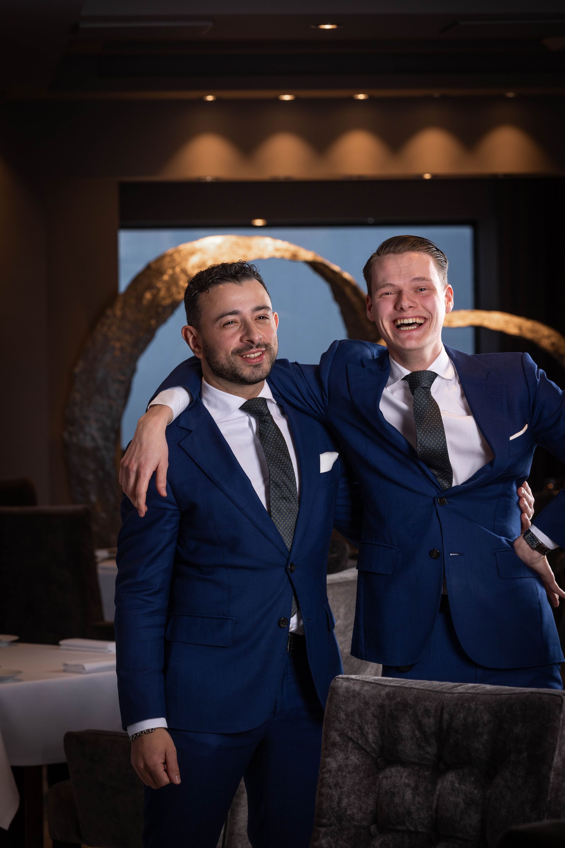 Twee mannen in pak en stropdas poseren voor een foto in een restaurant.