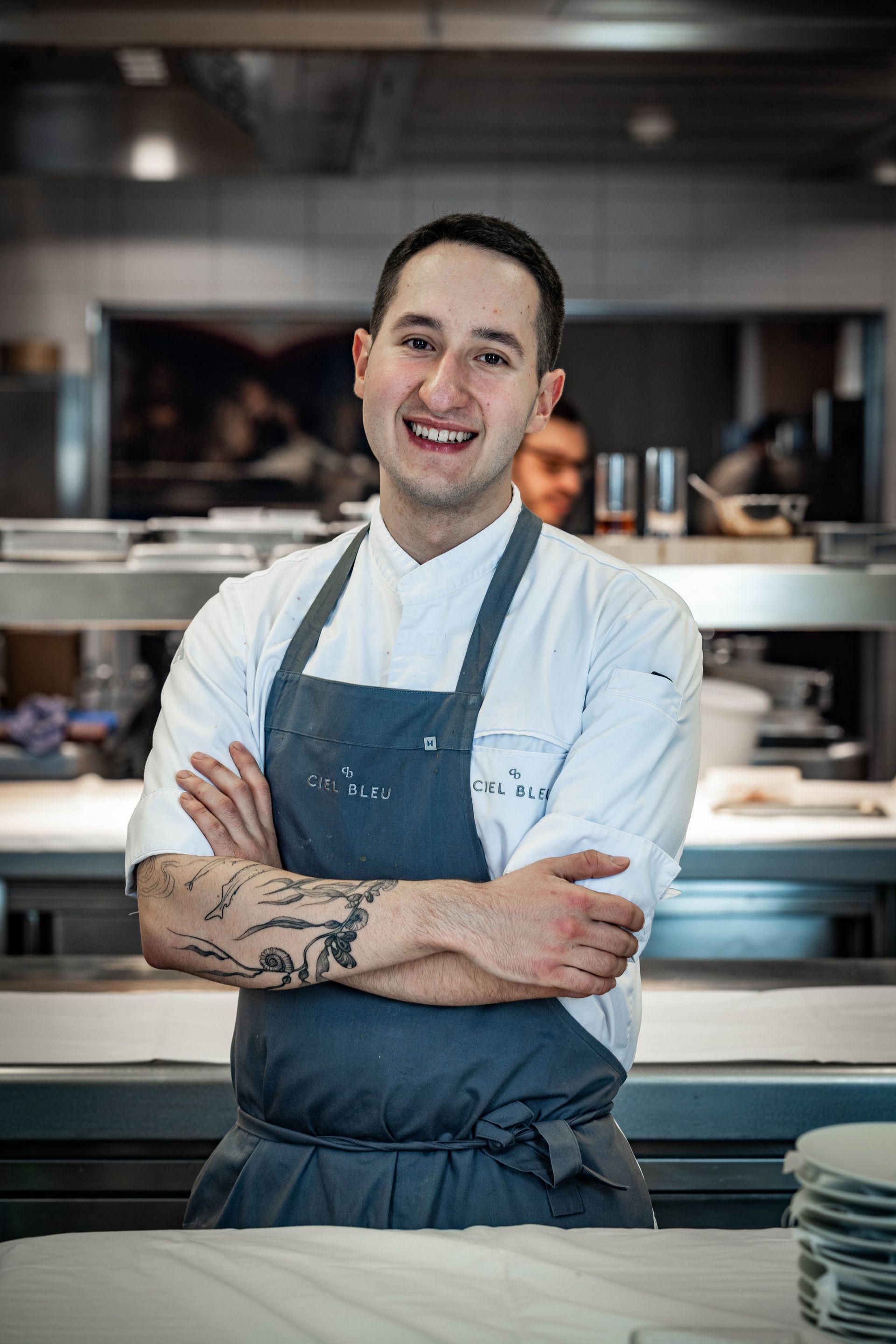 Een man met een schort staat in de keuken met zijn armen over elkaar.