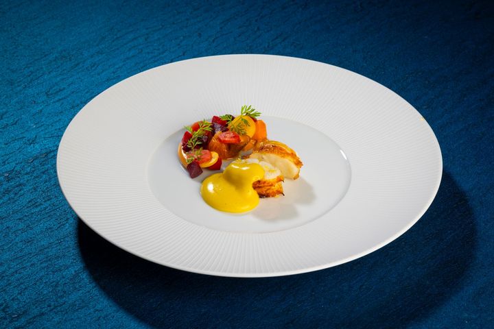 Gourmet fish dish on a swirl-patterned plate with green garnish and sauce on a blue surface.