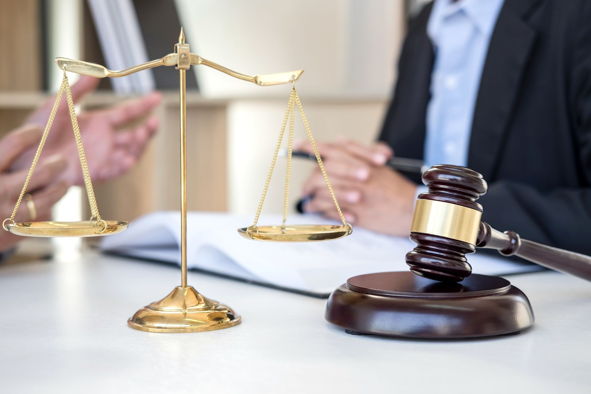 Une balance et un marteau de juge sur un bureau, deux personnes en costume, l'une gesticulant, discutant de documents.