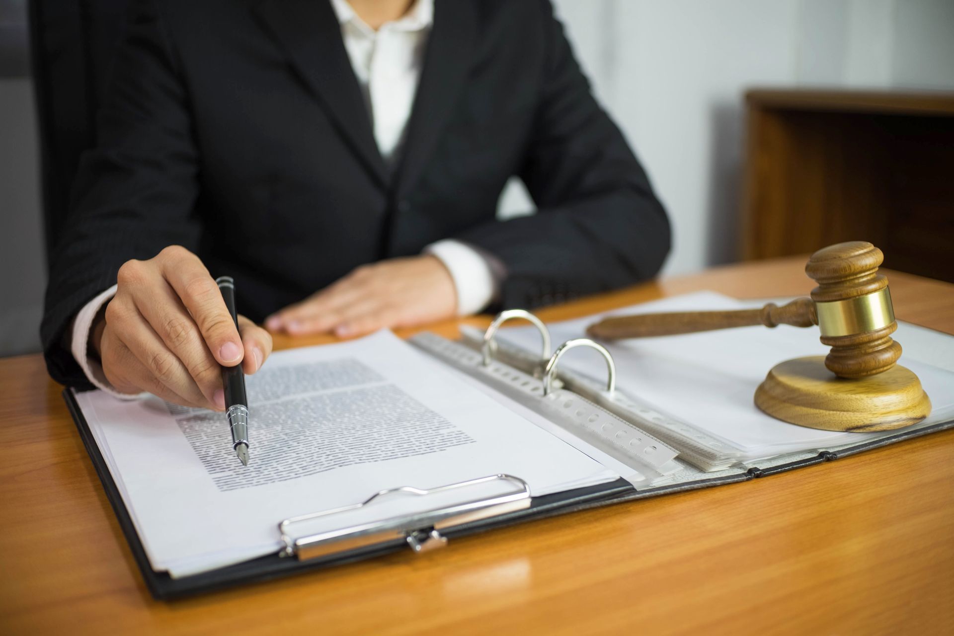 Person in suit points pen at document on desk with gavel.