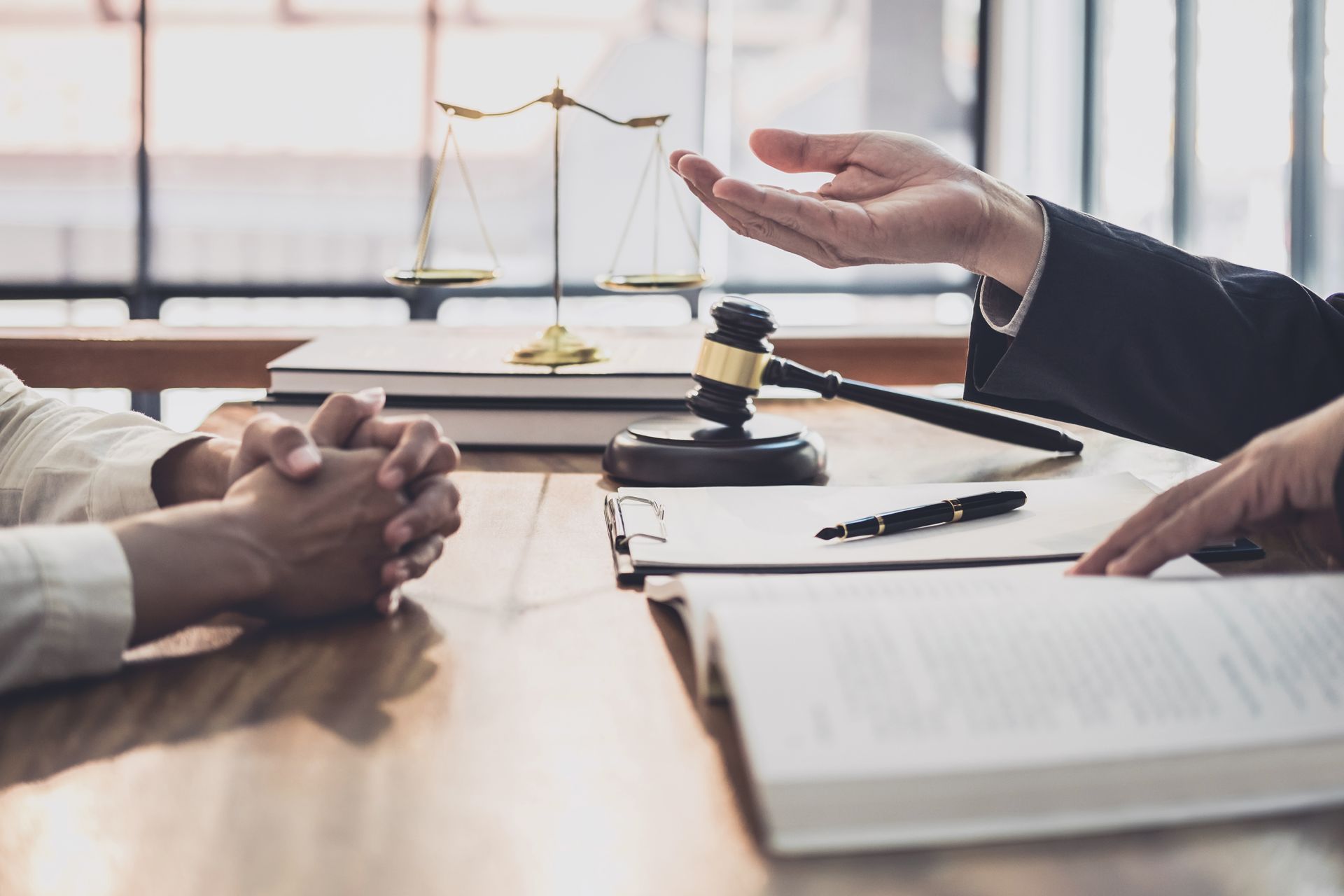 Lawyer gestures towards client with documents, gavel, and scales of justice on the table.