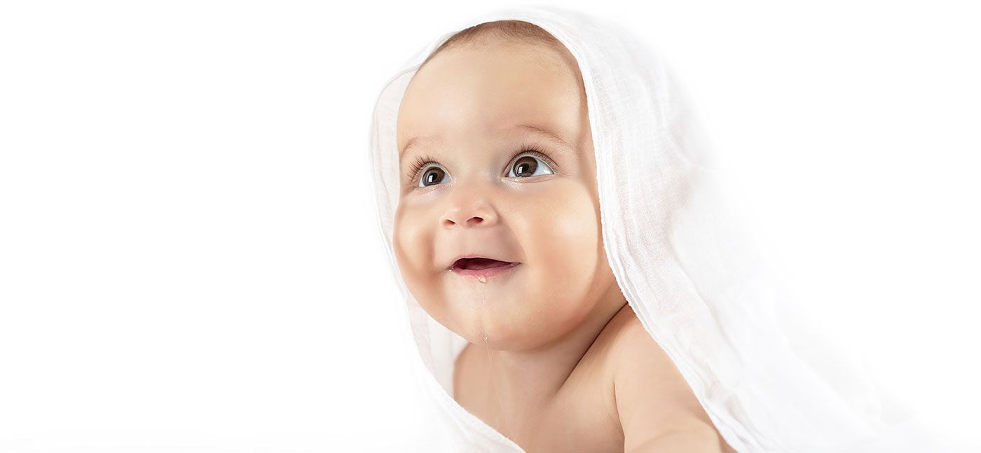 Baby wrapped in a white towel, smiling, looking upward.