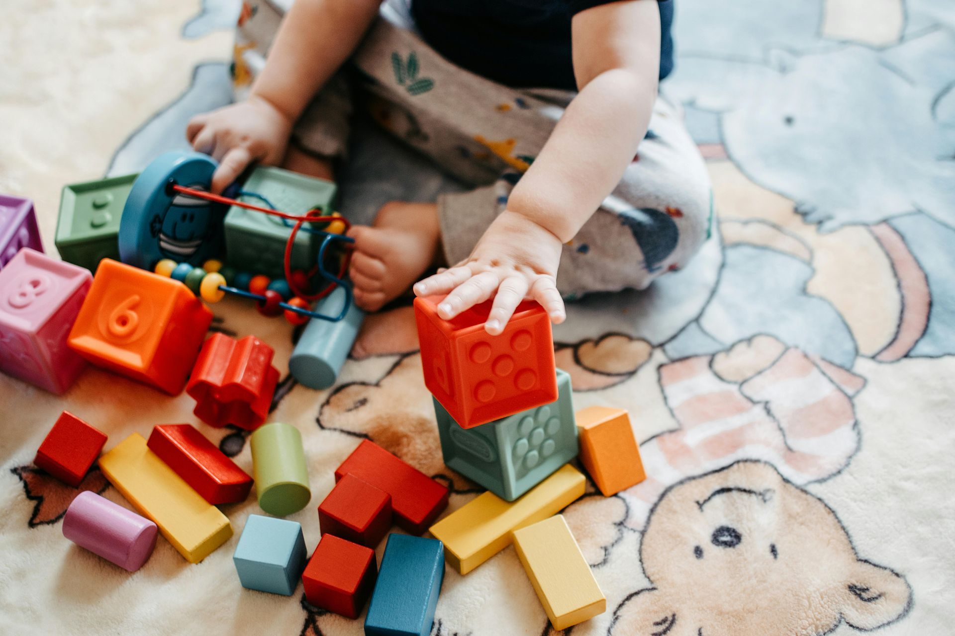 Child playing with colorful wooden blocks on a patterned blanket.