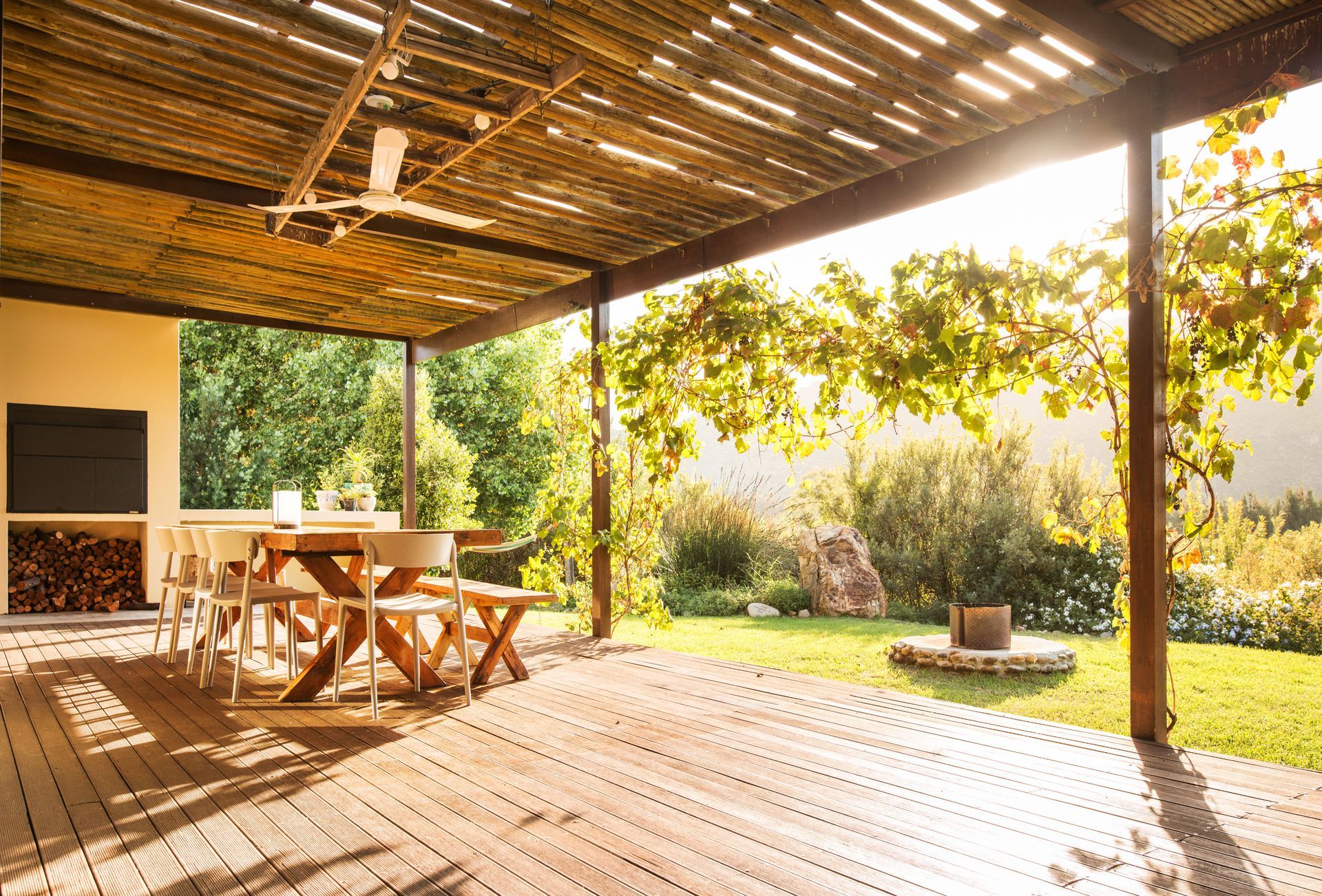 A wooden deck with a table and chairs under a pergola.
