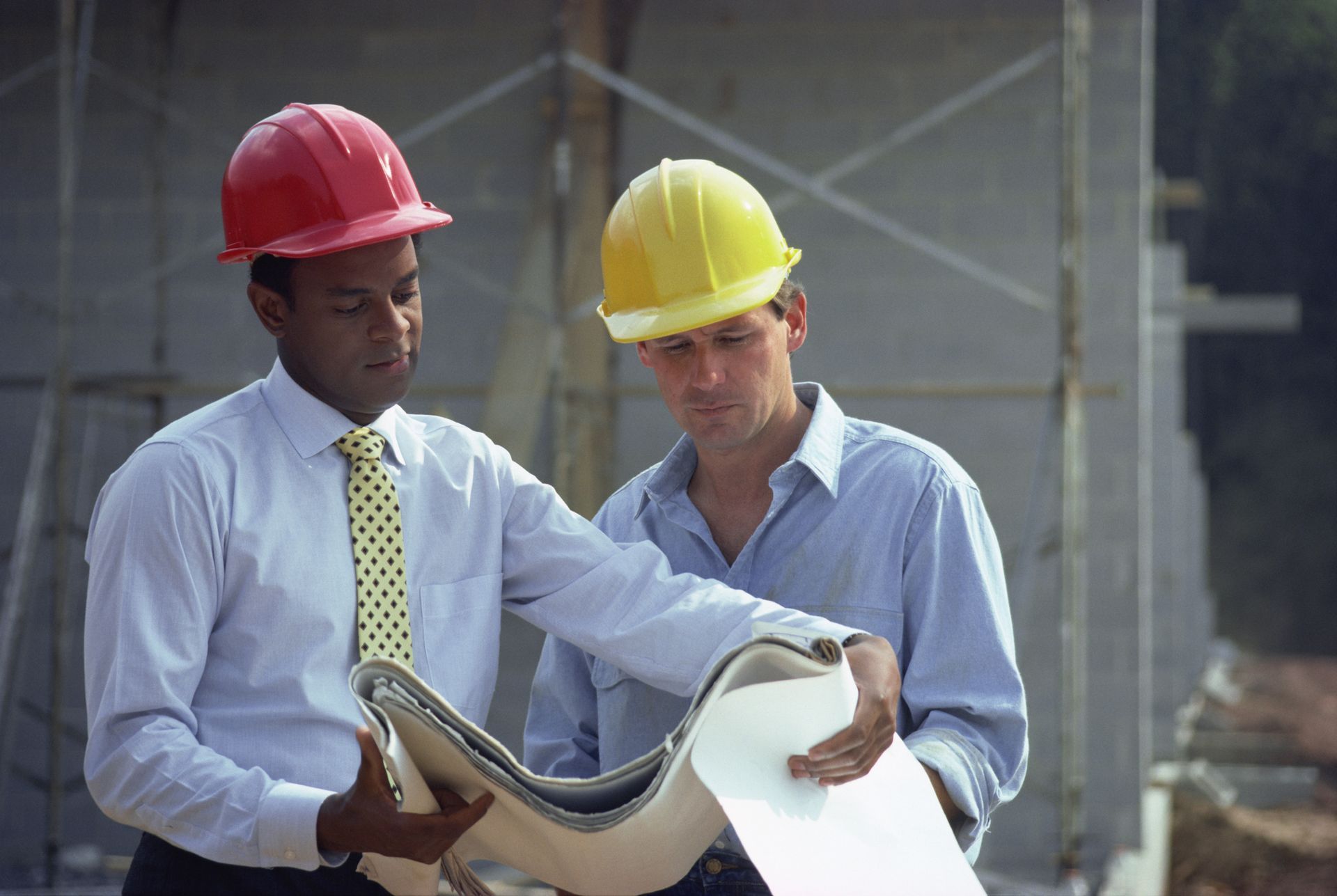Two men wearing hard hats are looking at a blueprint.