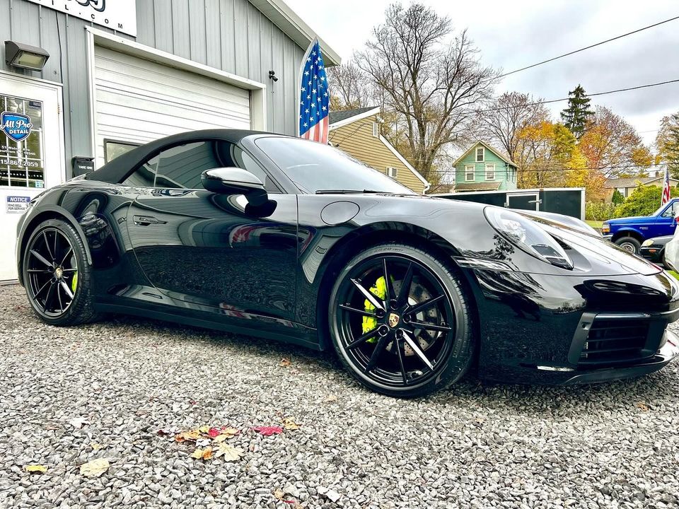 Black Porsche convertible with lime green brake calipers parked in front of a garage.