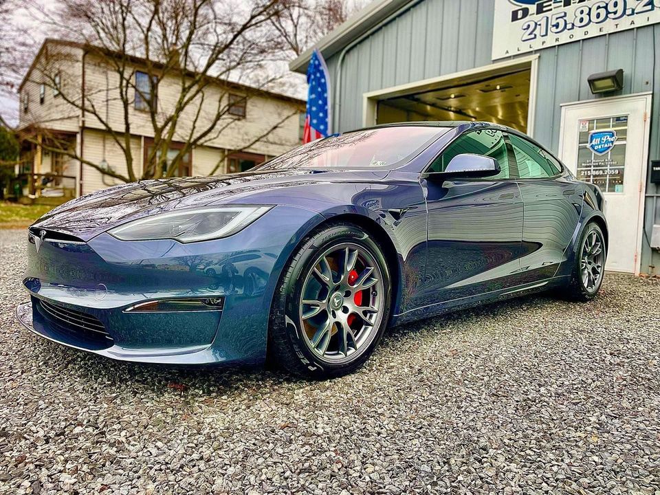 Blue Tesla car parked in front of a building with gravel ground.