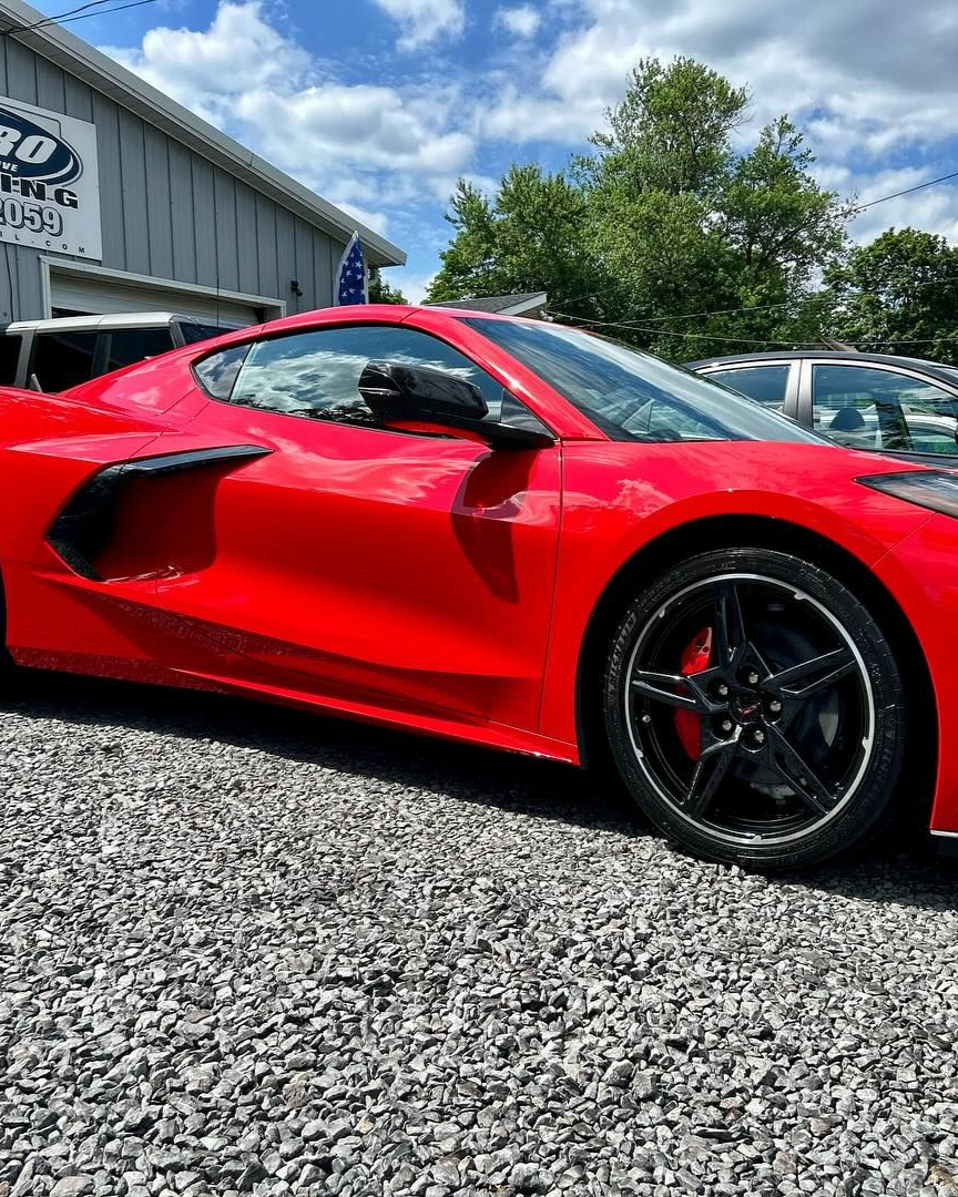 A person is using a blue squeegee to remove plastic from the hood of a car