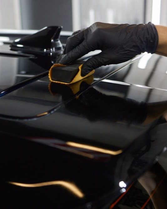 A person is using a blue squeegee to remove plastic from the hood of a car