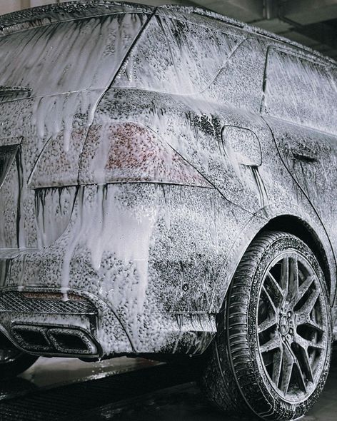 Car covered in white foam at a car wash. Rear of the vehicle is visible with taillights and a tire.