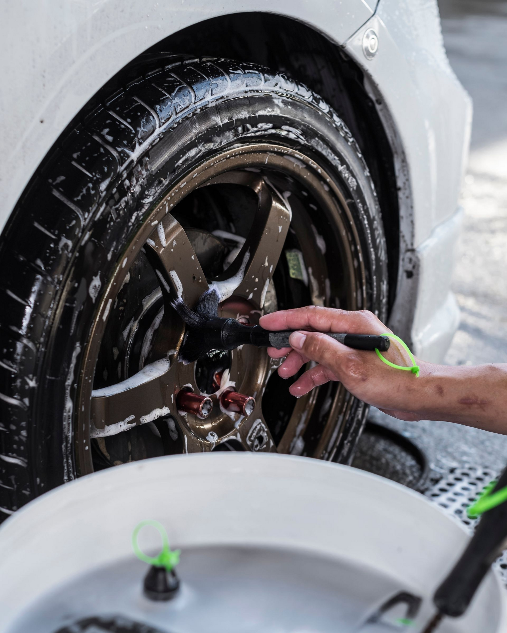 A person cleaning a car's bronze wheel with a brush and soapy water.