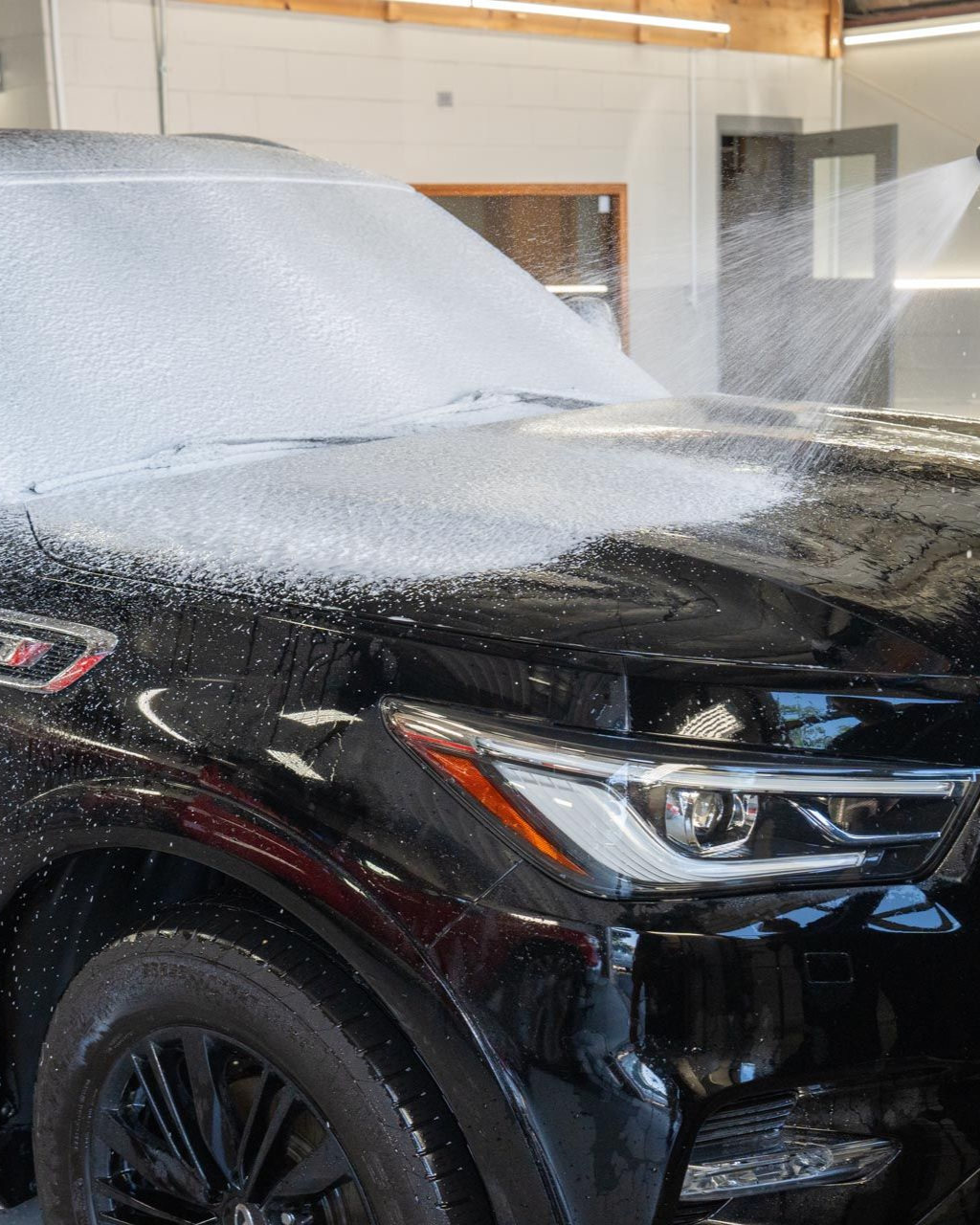 A person is using a blue squeegee to remove plastic from the hood of a car