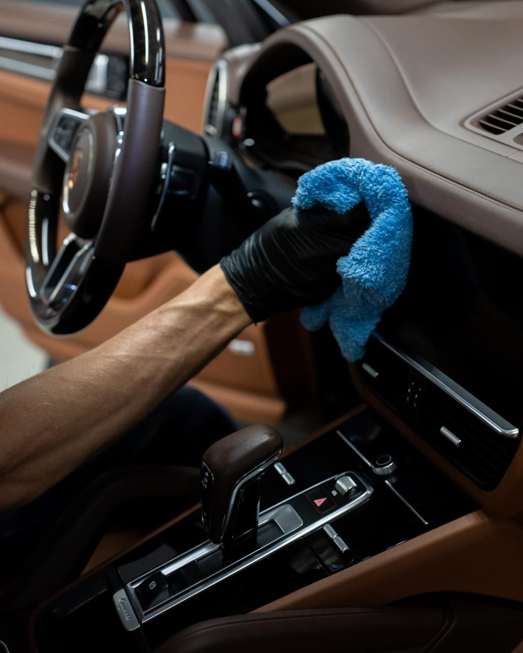 Person in black gloves cleans a tan car interior with a blue cloth.